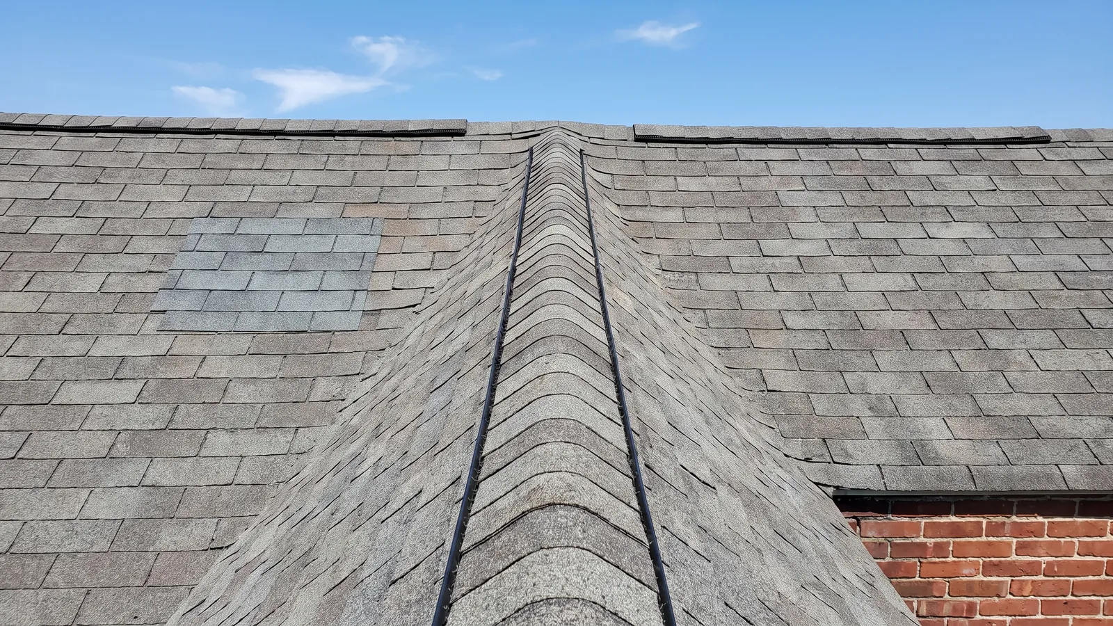Shingle-over ridge vent running along the peak of an asphalt roof, with two box vents removed and patched