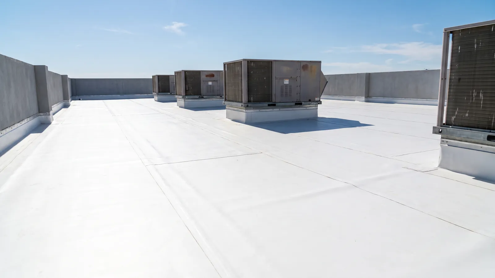 Bright white TPO membrane flat roof on a small commercial building with rooftop HVAC units and heat-welded seams